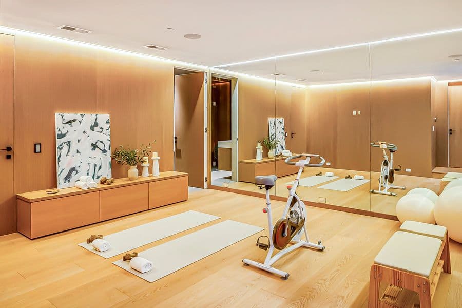 Home gym in Malibu (Larkspur Lane) with oak wall paneling, a long floating oak bench cabinet, a mirrored wall and a cove-lit ceiling